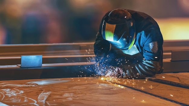 Een lasser met een zwart-geel masker voert werkzaamheden uit met een migmag-lasapparaat laswerkzaamheden