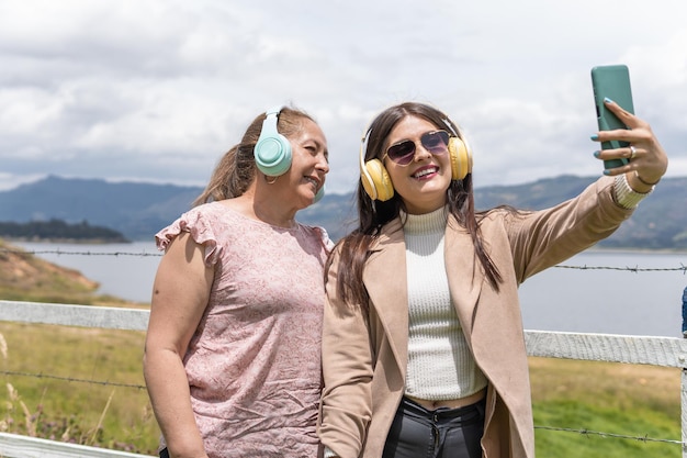 Een Latijnse jonge volwassen vrouw en haar moeder luisteren naar muziek en maken een selfie bij een meer