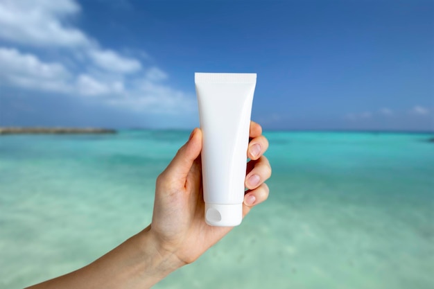 Een leeg buisje in de hand van een vrouw tegen de achtergrond van de turquoise oceaan of de zee op de Malediven Een mockup van een cosmetische crème of gel