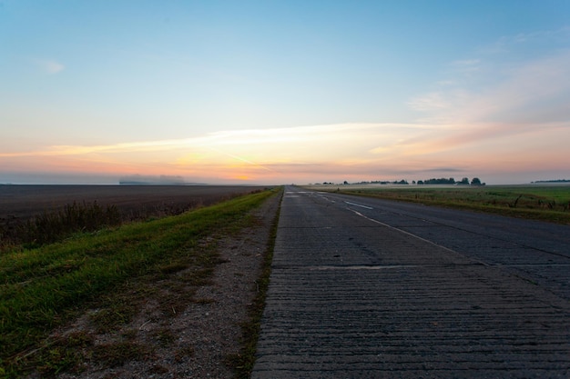 Een lege asfaltweg door de velden en bossen in een dikke mist bij zonsopgang