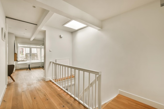 Een lege kamer met houten vloeren en witte muren. Er is een trap die naar de tweede verdieping leidt aan de rechterleuning