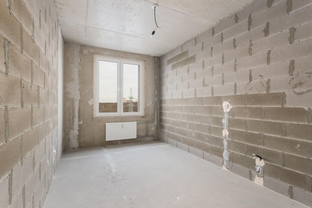Een lege kamer zonder decoratie, met muren van schuimblokken en een raam met uitzicht op een hoogspanningsmast.