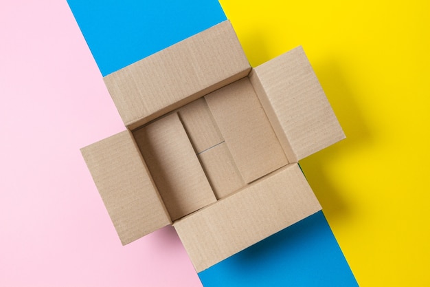 Een lege open kartonnen doos op geometrische roze, blauwe, gele achtergrond. Bovenaanzicht, kopieer ruimte