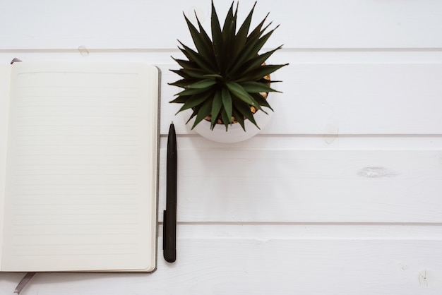 Een lege witte notebook op een witte houten tafel met bloempot