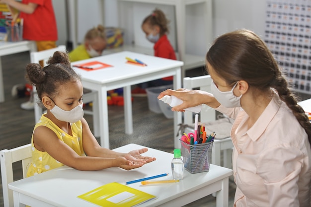 Een leraar helpt een afro-amerikaanse student met handreiniging in de klas.