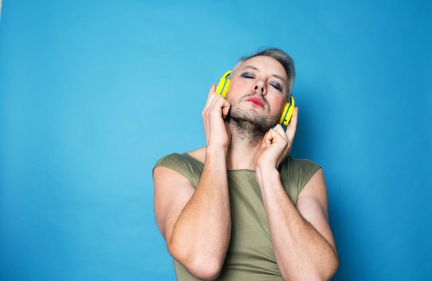 Een Lgbt-transseksuele man met lichte make-up op zijn gezicht luistert naar muziek in een gele koptelefoon die op een geïsoleerde achtergrond staat