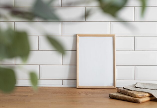 Een licht frame met een leeg doek tegen een witte tegelwand en op een houten tafel