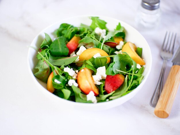 Een lichte zomerse salade van rucolla-perziken en kaas op een lichte ondergrond