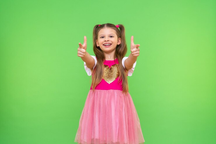 Een lief vrolijk meisje wijst haar vingers naar voren Een kind op een groene geïsoleerde achtergrond
