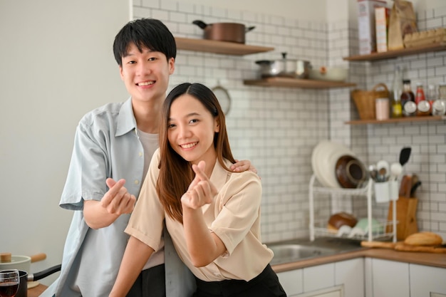 Een liefdevol Aziatisch stel is in de keuken en maakt een mini-harthandteken glimlachend en kijkend naar de camera