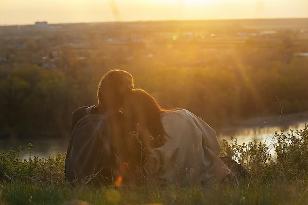 een liefdevol paar omarmen zit op een hoge oever van de rivier in de zonsondergangstralen van de zon