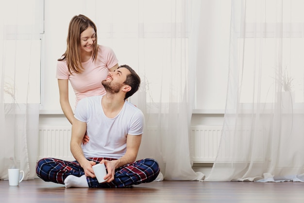 Een liefdevol stel lacht op de grond tegen het raam in de kamer