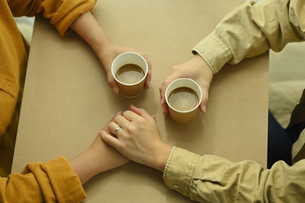 Een liefhebbend jong koppel dat handen vasthoudt op tafel met koffiekopjes Liefdesrelatie en levensstijlconcept