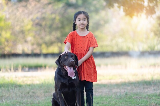 Een lieflijk Zuidoost-Aziatisch kindmeisje in rode outfits speelt 's avonds met haar grote hond in de voor- of achtertuin. Dierenliefhebber concept