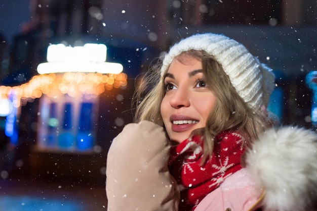 Een lieftallige dame op straat in een winterjas lacht vrolijk rond de avondlichten van de stad