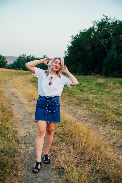 Een lieve jonge gelukkige vrolijke mooie vrouw die op een mooie zomerdag buiten in het park loopt Het meisje luistert naar muziek met een koptelefoon