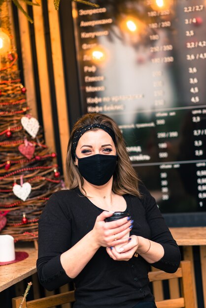 Een lieve vrouw met een kaukasisch uiterlijk in een zwart gezichtsmasker, zit en werkt in een internetcafé.