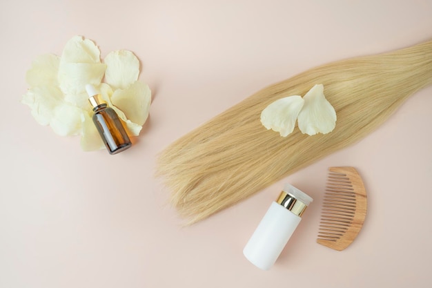 Een lok blond haar een druppelflesje natuurlijke etherische olie voor haarbehandeling en een houten kam