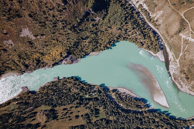 Een luchtfoto genomen vanuit een helikopter van een berglandschap, een turquoise stroom stroomt tussen twee oevers met veel bomen.