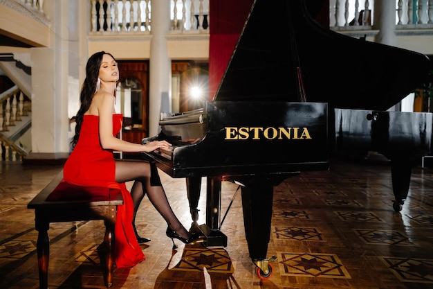 Een luxe actrice in een rode jurk speelt piano in de grote zaal van het theater