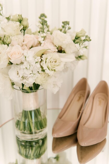 Een luxe bruidsboeket met witte rozen naast schoenen en accessoires op een lichte achtergrond