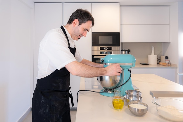 Een man-bakker die thuis een roodfluwelen cake kookt en de cake voorbereidt in de keukenrobot die thuis werkt