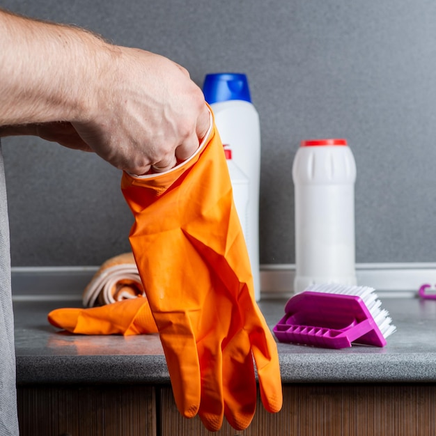 Een man bereidt zich voor om de keuken schoon te maken Trekt een rubberen handschoen aan tegen de achtergrond van schoonmaakbenodigdheden op de keukentafel