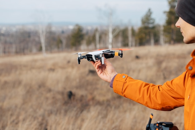 Een man bestuurt een quadcopter-drone buiten in de herfst. De man steekt zijn hand uit naar de drone.