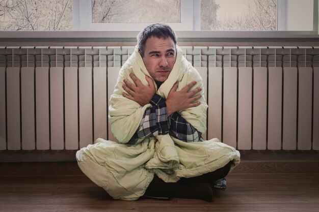 een man bevriest in een kamer van zijn appartement tijdens de winterperiode Het uitschakelen van de verwarming Problemen met centrale verwarming