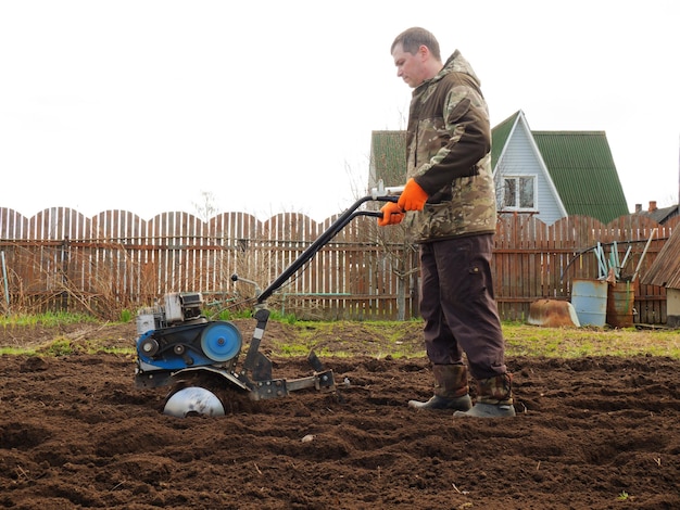 Een man bewerkt het land in de tuin met een cultivator en bereidt de grond voor op het zaaien van landbouwconcept