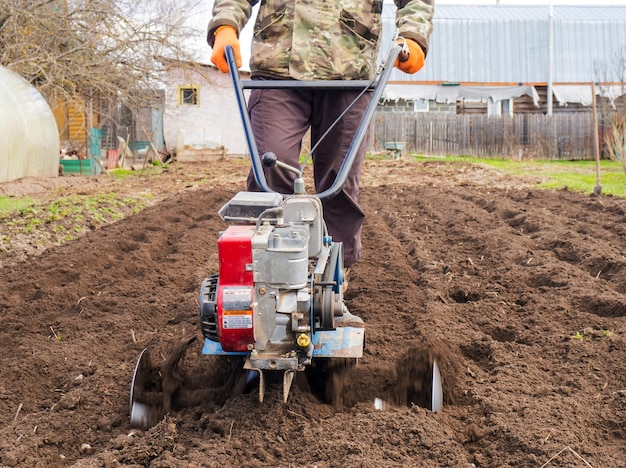 Een man bewerkt het land in de tuin met een cultivator en bereidt de grond voor op het zaaien van landbouwconcept