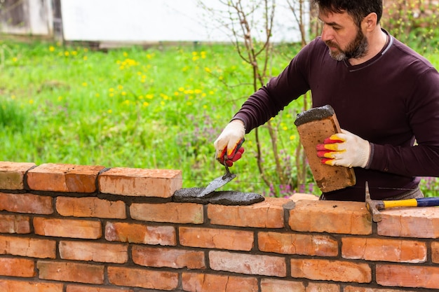 Een man bouwt een muur van bakstenen, legt een baksteen op een cementzandmortel