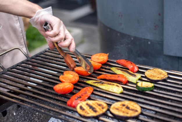 Een man braadt groenten op een grill met kolen