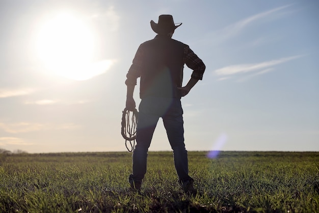 Een man cowboyhoed en een loso in het veld. Amerikaanse boer in een veld met een jeanshoed en een loso. Een man loopt over het veld silhouet