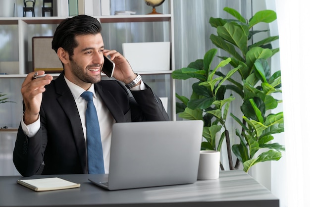 Een man die aan het telefoneren is terwijl hij aan een bureau zit met een laptop.