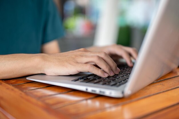 Foto een man die aan zijn laptop werkt en op het toetsenbord van de laptop schrijft, zit aan een buitentafel van een café