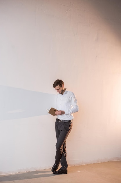 Een man die bij de witte muur staat en een boek leest