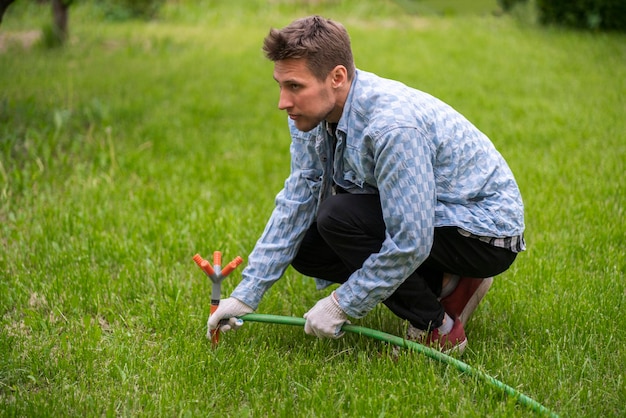 Een man die een graswatersproeier vasthoudt en het atomaire bewateringssysteem aanpast