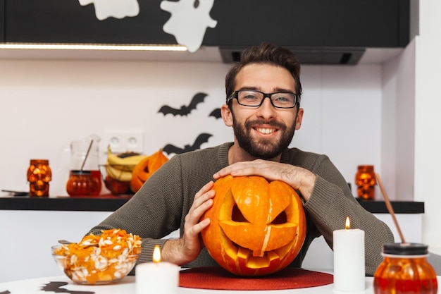 Een man die een Halloween-pompoen knuffelt, kijkt naar de camera en glimlacht