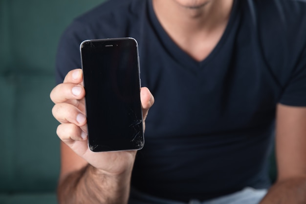 Een man die een kapotte telefoon vasthoudt terwijl hij op de bank zit