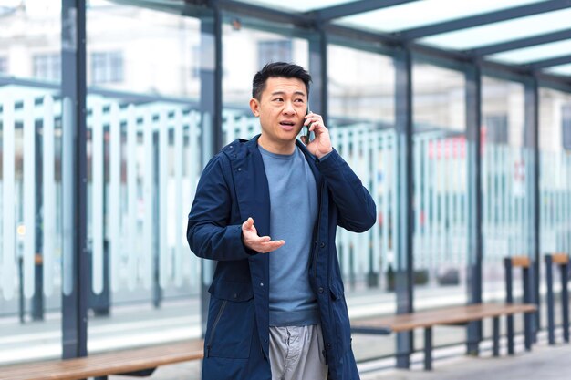 Een man die gefocust en serieus aan de telefoon praat bij een openbaar vervoer stopt een zakenman in de buurt van het kantoorcentrum