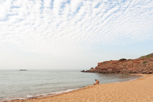 Een man die op een strand in Menorca zit, beoefent nudisme