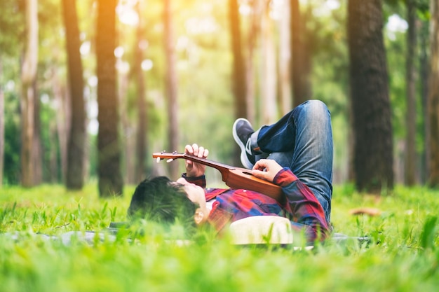 Een man die ukelele speelt terwijl hij op een groene tuin ligt