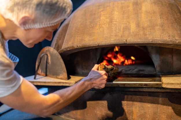 Een man die vuur maakt in de oven in de Italiaanse bakkerij