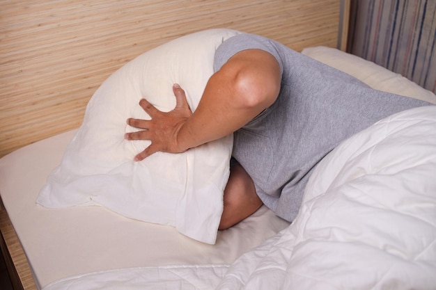 Een man die zijn hoofd bedekt met een kussen dat zich bang of depressief voelt, lijdt aan slapeloosheid