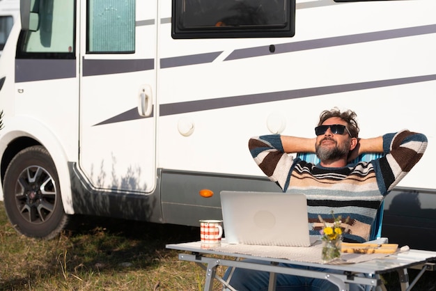 Een man digitale nomade levensstijl bezig met alternatief buiten werkplek bureau met een camper camper op de achtergrond Mensen en kantoorvrijheid Modern klein zakelijk concept baanreiziger