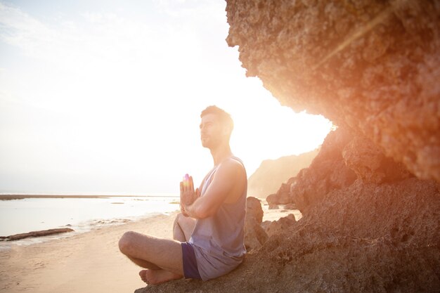 Een man doet yoga bij zonsondergang op de rotsen