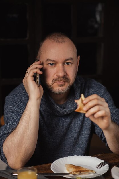 Een man eet een broodje en spreekt aan de telefoon Gewone man van middelbare leeftijd Eten met een telefoon in de hand