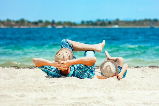 Een man en een kind liggen op het strand en de zee is blauw en de lucht is blauw.