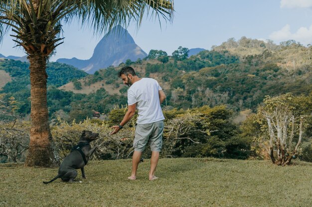 Een man en een Pit Bull-hond spelen en bewonderen de natuur en de bergen van PetrÃ,polis, in Rio de Janeiro, Brazilië. Liefdevolle relatie tussen mens en dier.